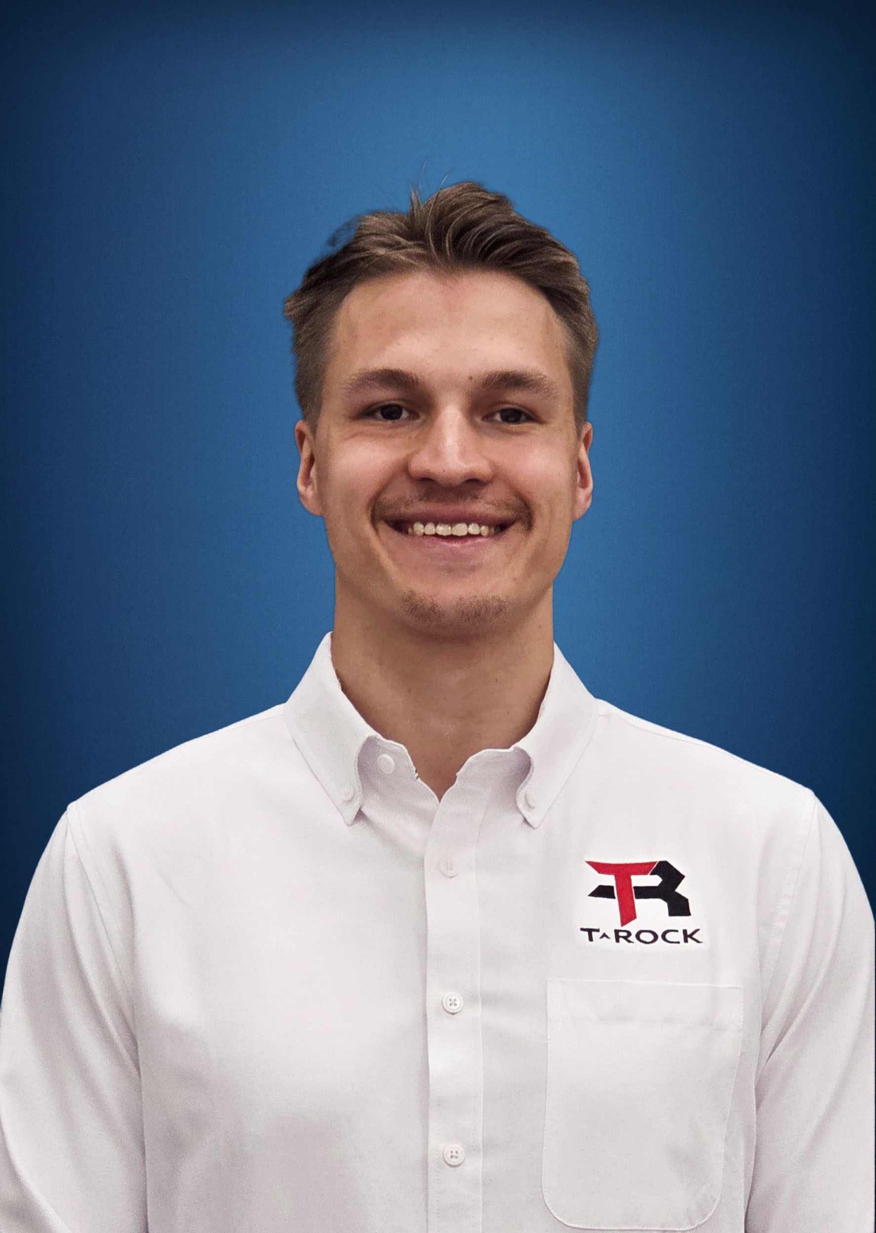 Smiling man in a white button-up shirt with a Tarock logo on the chest, blue backdrop behind him.