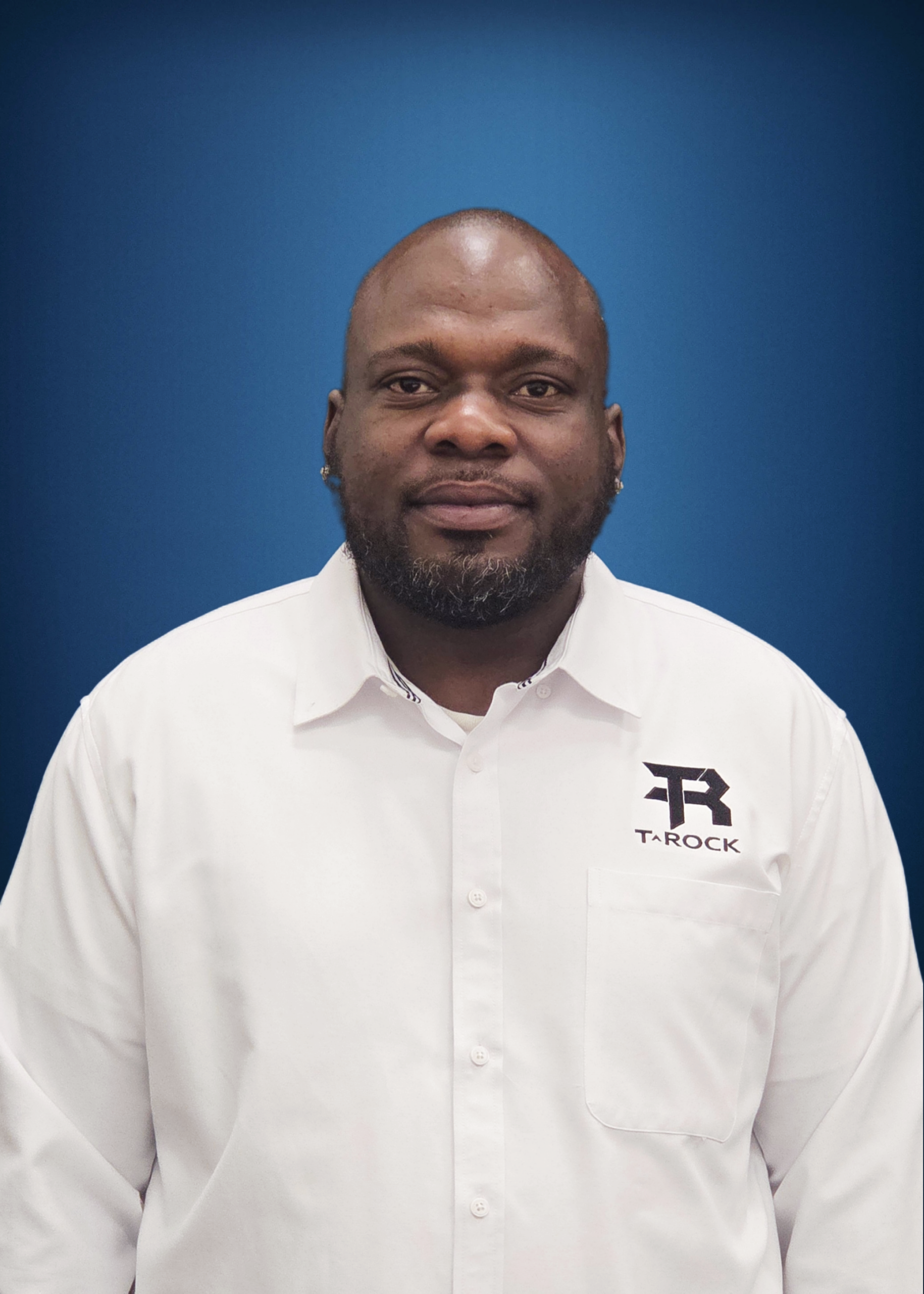 Head-and-shoulders portrait of a man with a short beard in a white collared shirt, blue gradient backdrop; TAROCK logo on left chest.